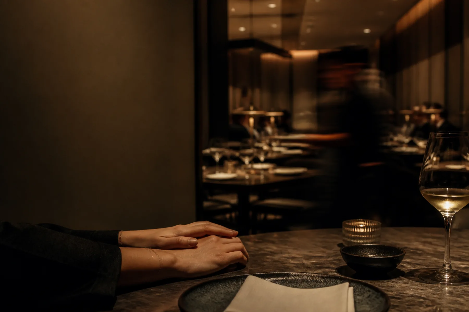 A closed laptop on a dining banquette beside a candle and a half-finished glass of wine.
